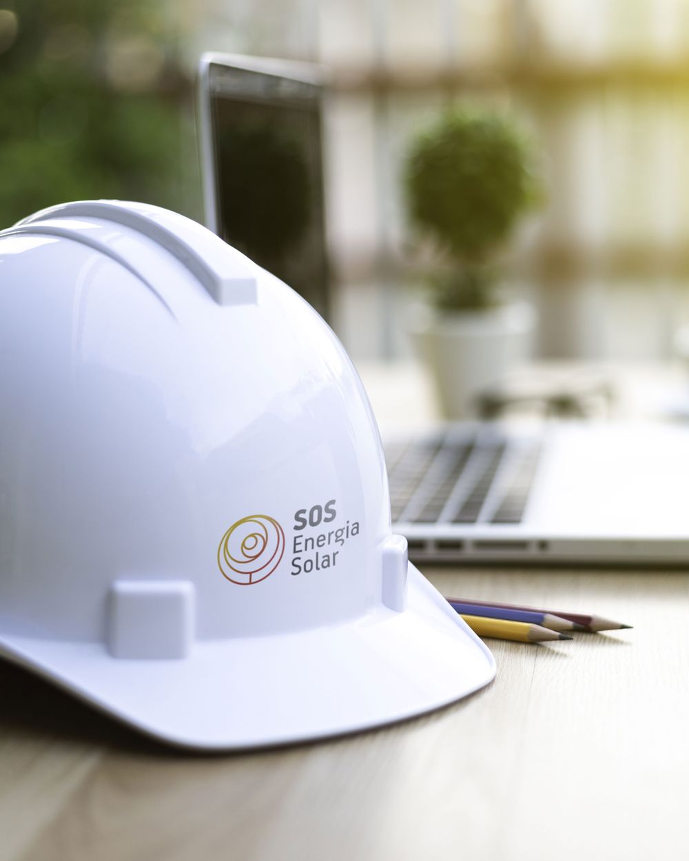 Capacete de segurança com a marca da SOS Energia Solar sobre a mesa de projetos
